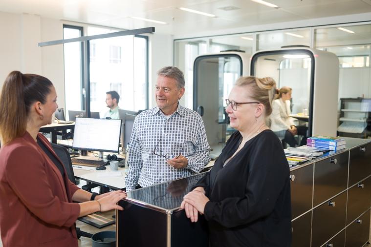 Mitarbeitende des Markenverbandes im flexiblen Büro mit Telefonboxen im Hintergrund.